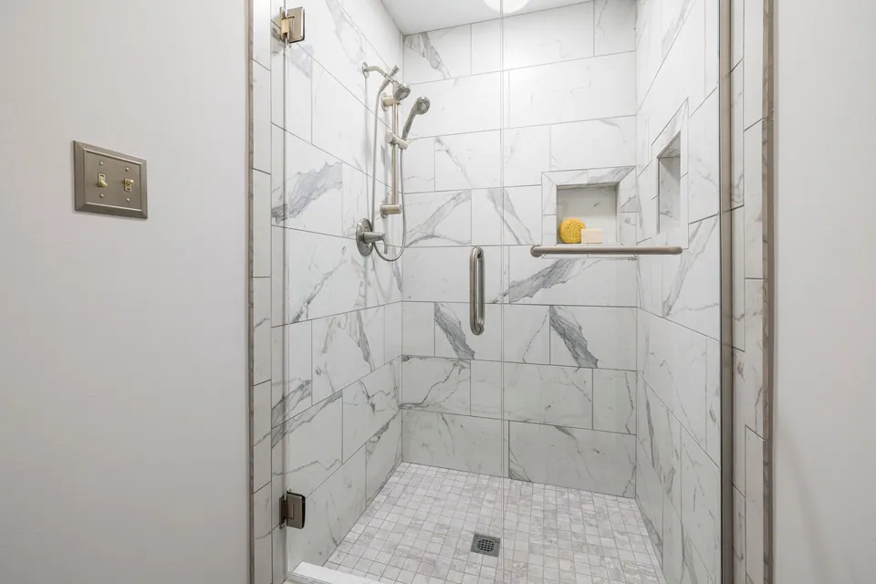 Douche finie avec carrelage clair, paroi vitrée et barre d’appui horizontale